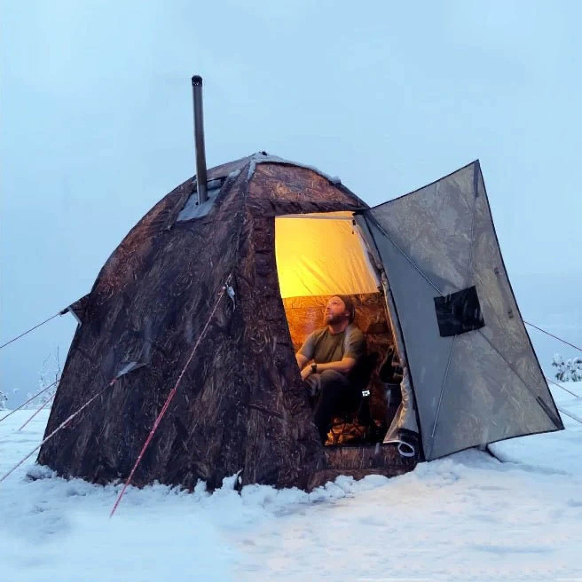 A man in an for season tent at a winter campsite